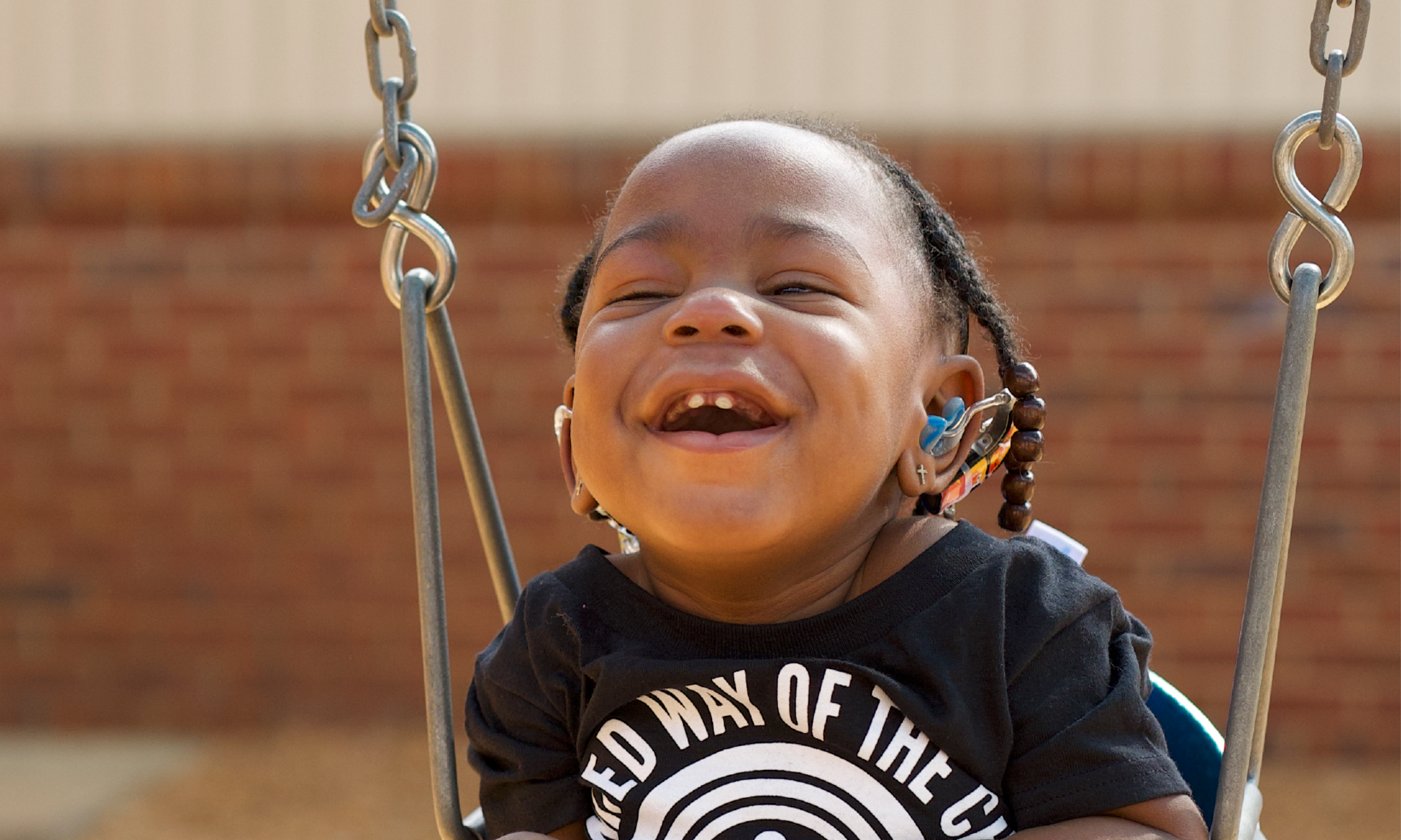 child with hearing aid laughing in swing