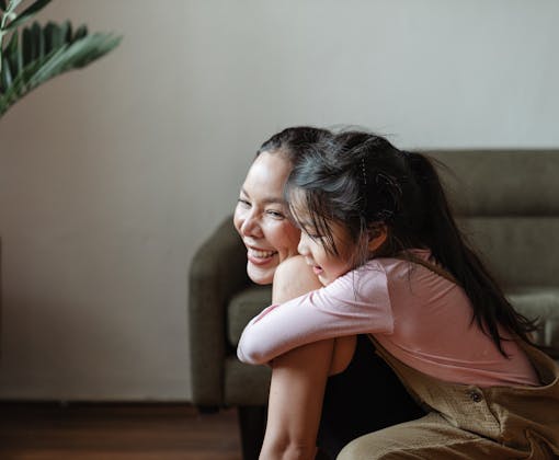 Smiling mother and daughter sharing a warm embrace in a cozy home setting.