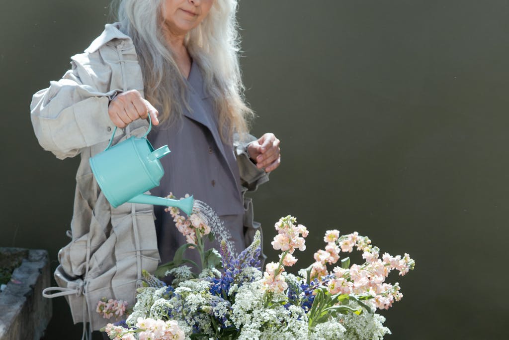 Elderly Caucasian woman watering a flower arrangement with a green watering can outdoors.