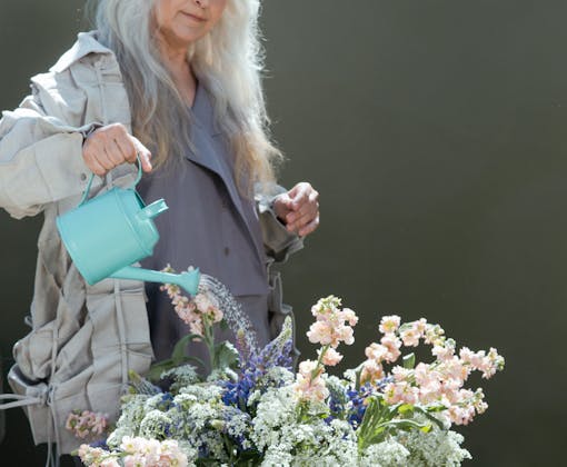 Elderly Caucasian woman watering a flower arrangement with a green watering can outdoors.