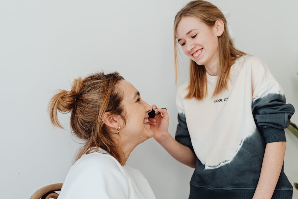 Happy mother and daughter enjoying a fun makeup session indoors.