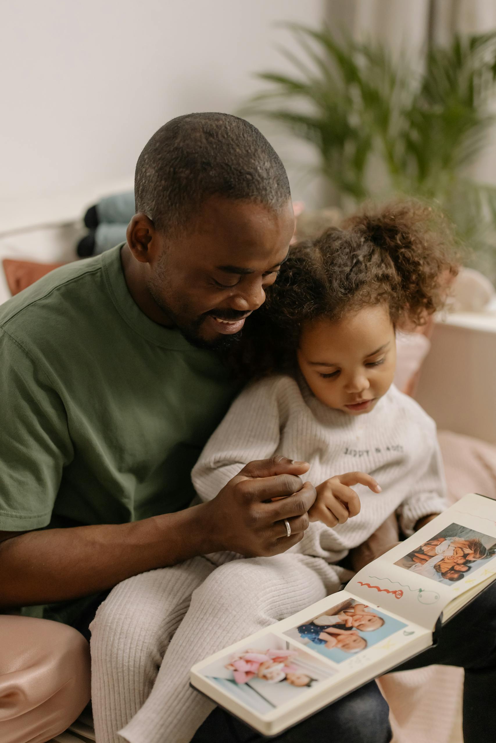 A father and daughter share a joyful moment browsing a family photo album together.