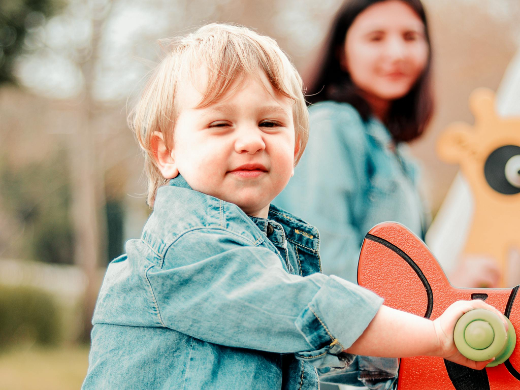 A joyful child in denim enjoys a sunny day at the park, riding a playground rocker.