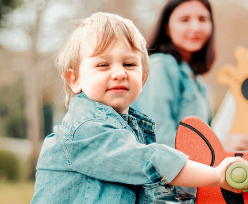 A joyful child in denim enjoys a sunny day at the park, riding a playground rocker.
