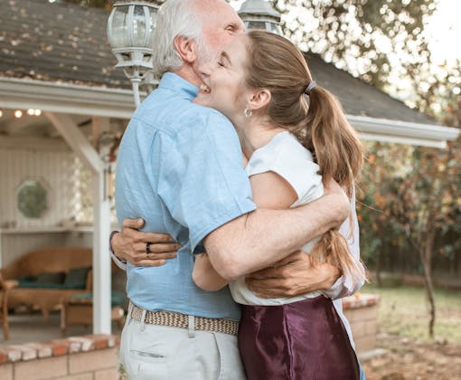 A touching moment between an elderly father and his adult daughter sharing an embrace in a garden.