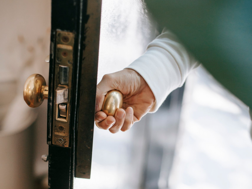 From above of crop anonymous person holding metal door handle while entering house in sunshine