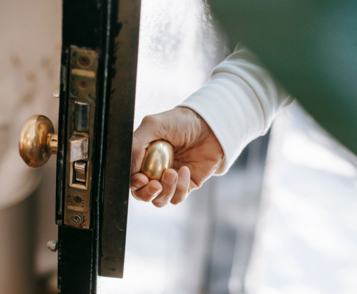 From above of crop anonymous person holding metal door handle while entering house in sunshine