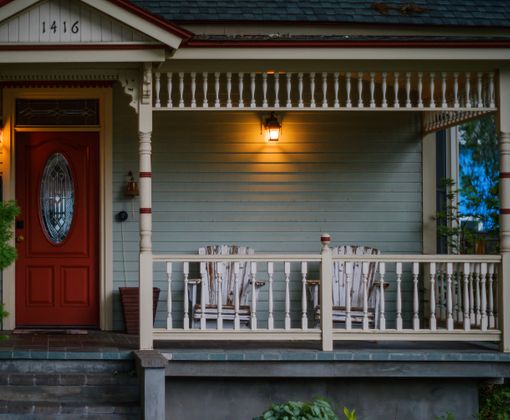Inviting porch with red door, wooden armchairs, and glowing lights, perfect for evening relaxation.