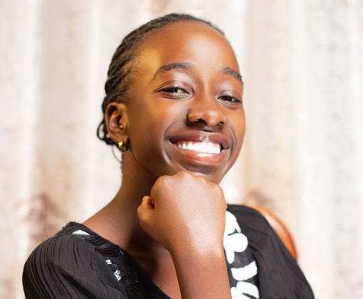 Portrait of a smiling teen girl in a black dress with a confident pose indoors.